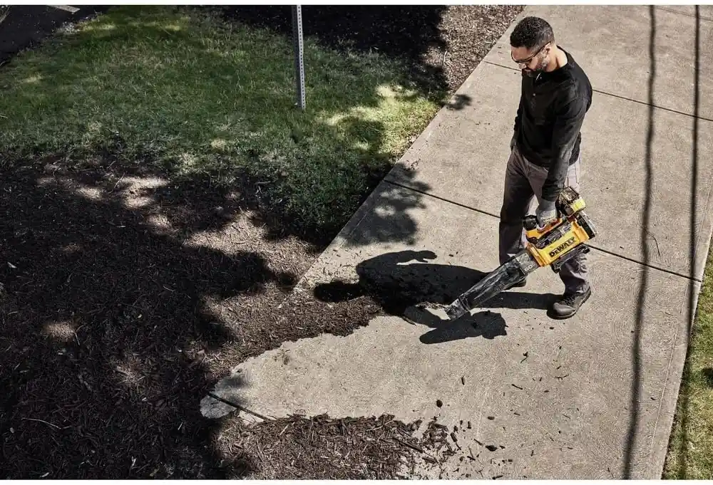 Man in a black jacket clearing mulch off a concrete walkway with the DEWALT 60V MAX FLEXVOLT blower