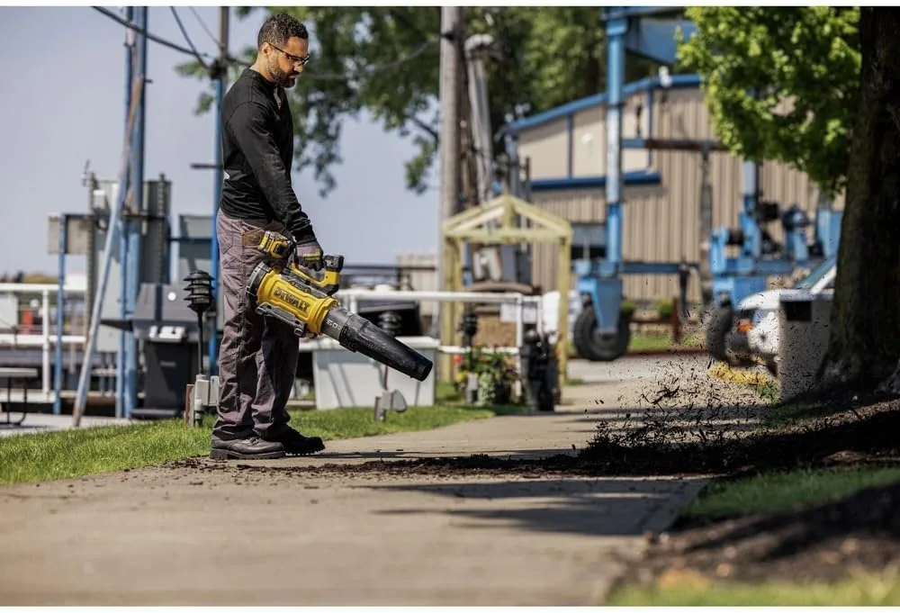 Man blowing leaf litter along a paved path with a yellow DEWALT 60V MAX FLEXVOLT handheld blower