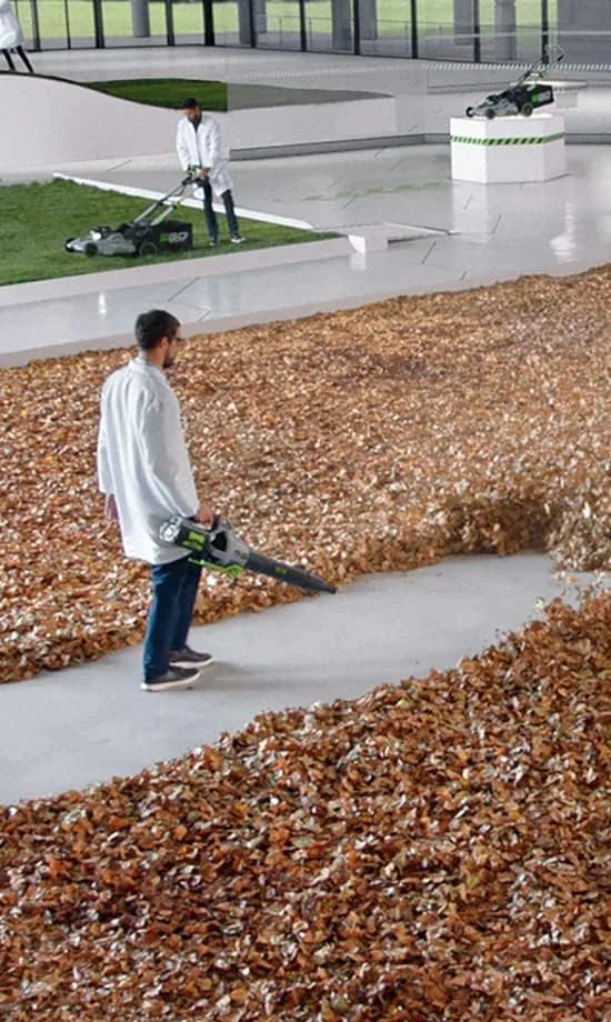 Man clearing a thick layer of fallen leaves off a concrete path with the EGO LB6504 cordless leaf blower