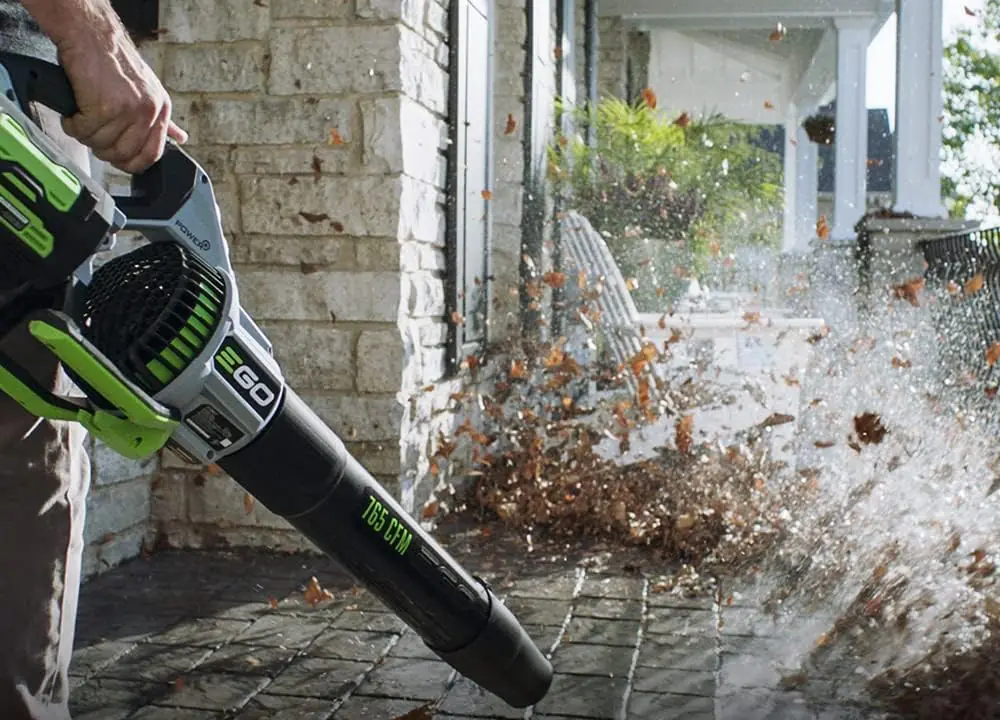Man using the EGO LB7654 cordless leaf blower to clear fallen leaves off a stone porch