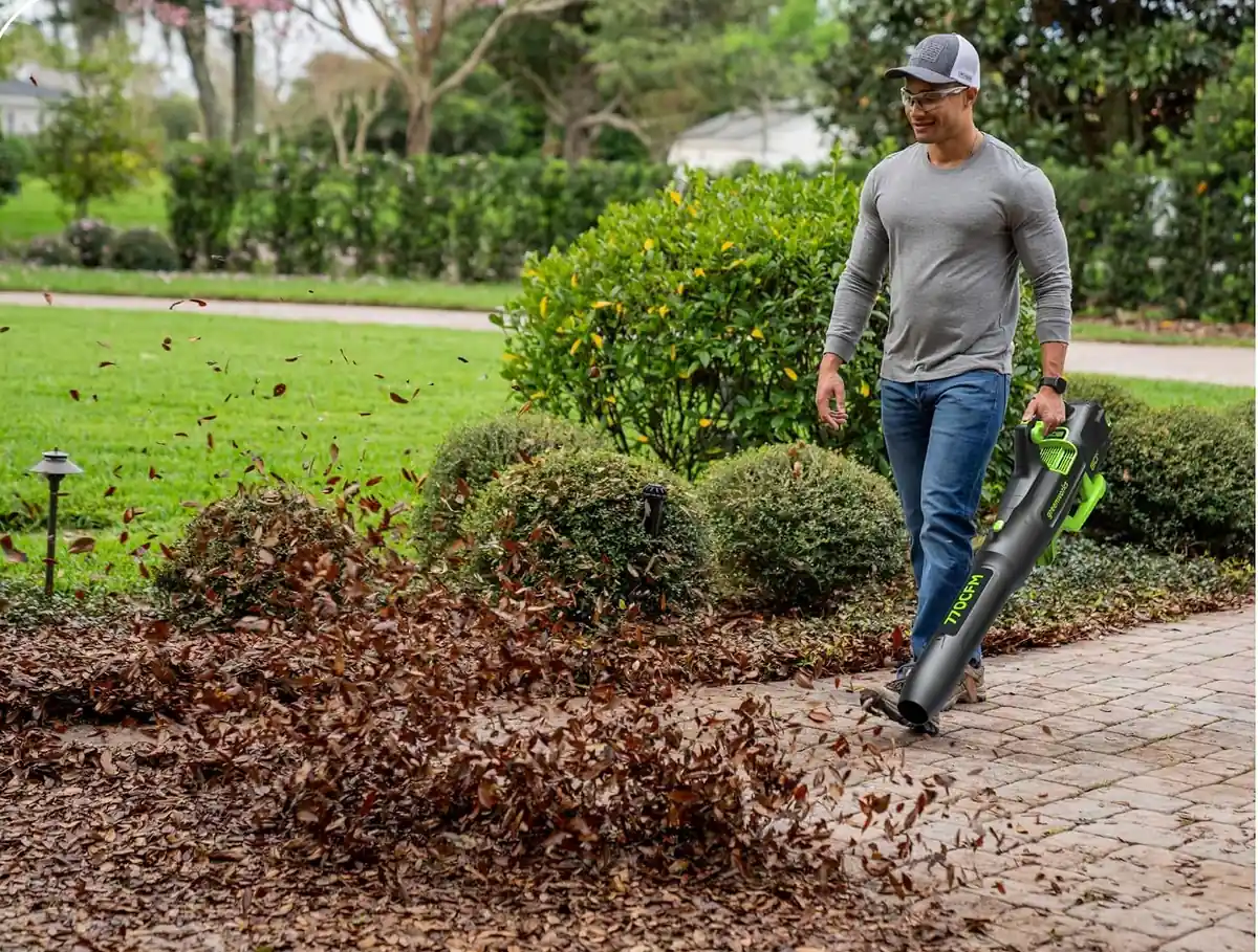 Man walking along a paved path blowing a pile of fallen leaves with a Greenworks 80V cordless leaf blower