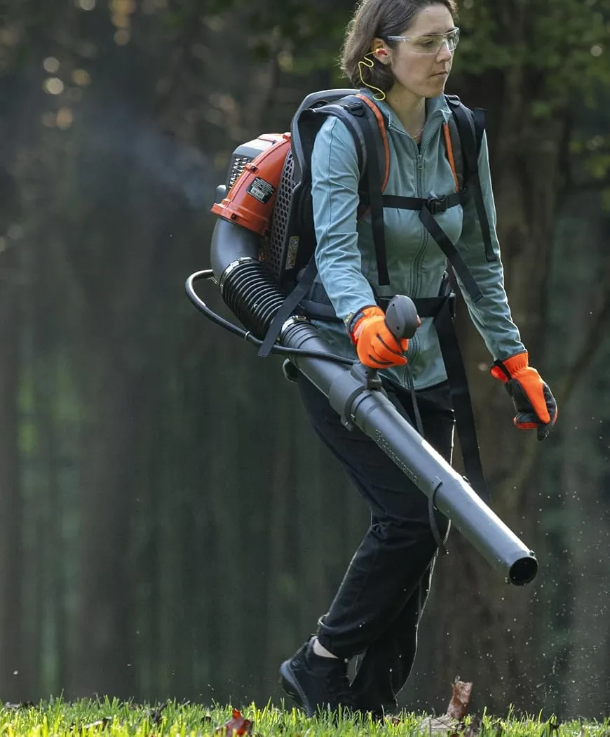 Woman in safety glasses and orange gloves clearing leaves on grass with the Husqvarna 150BT backpack blower