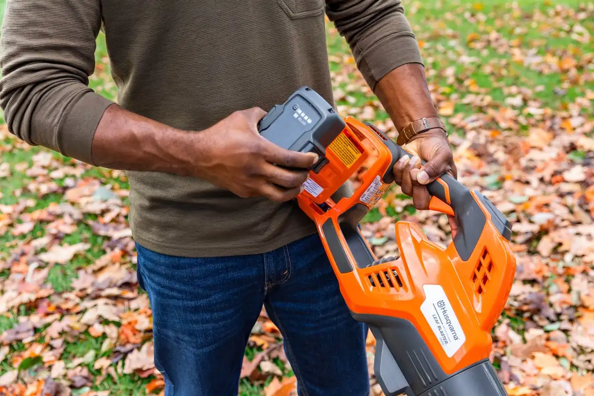 Man fitting the battery into a Husqvarna 350iB blower over a lawn covered in autumn leaves