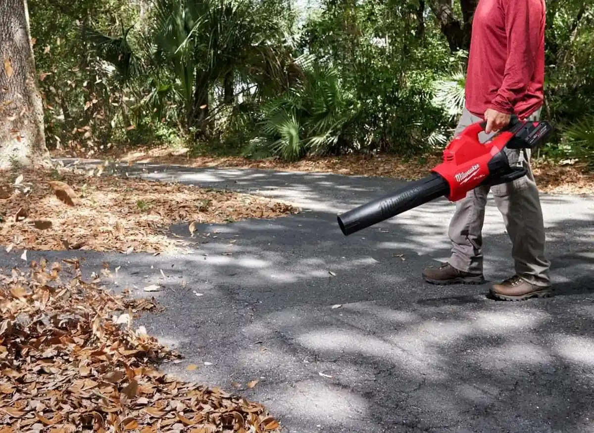 Man in a red shirt blowing dry leaves off an asphalt driveway with the Milwaukee dual battery blower