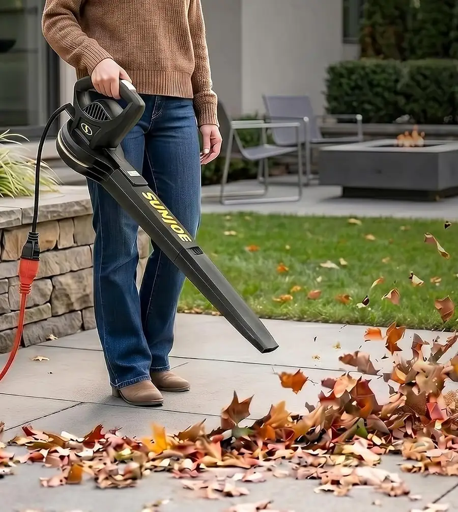 Woman clearing fallen leaves off a stone patio with the Sun Joe corded electric leaf blower