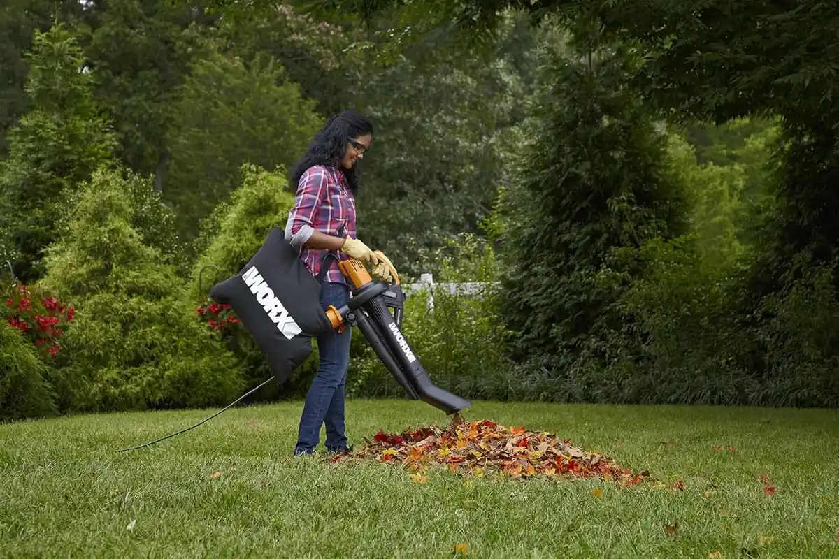 Woman in gloves and safety glasses vacuuming a pile of autumn leaves with the WORX Trivac and its shoulder bag