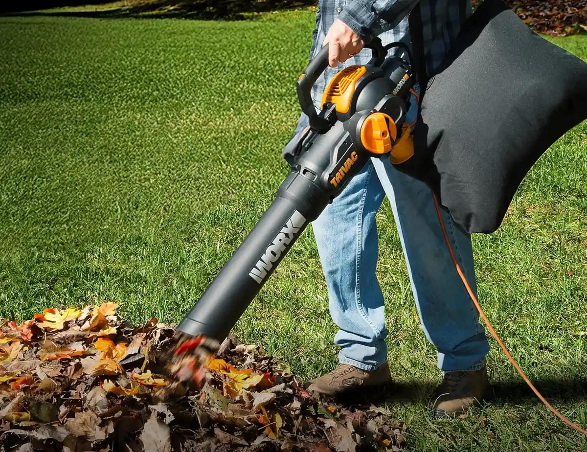 Man vacuuming a pile of fall leaves on a lawn with the WORX Trivac WG512 and its shoulder bag