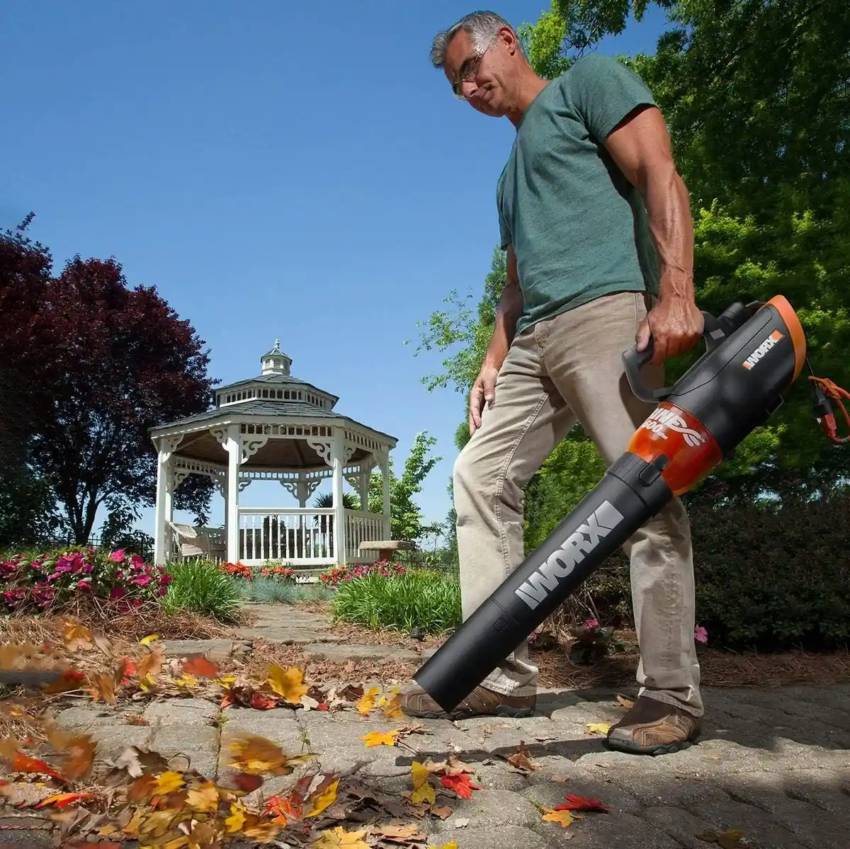 Man blowing autumn leaves off a garden path with the WORX WG520 corded leaf blower