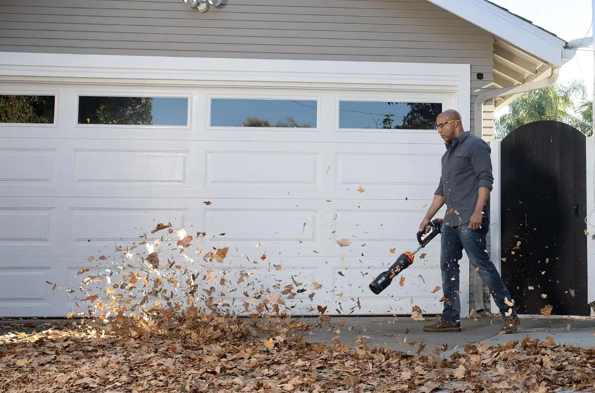 Man blowing a large pile of leaves across a driveway with the WORX 20V cordless leaf blower